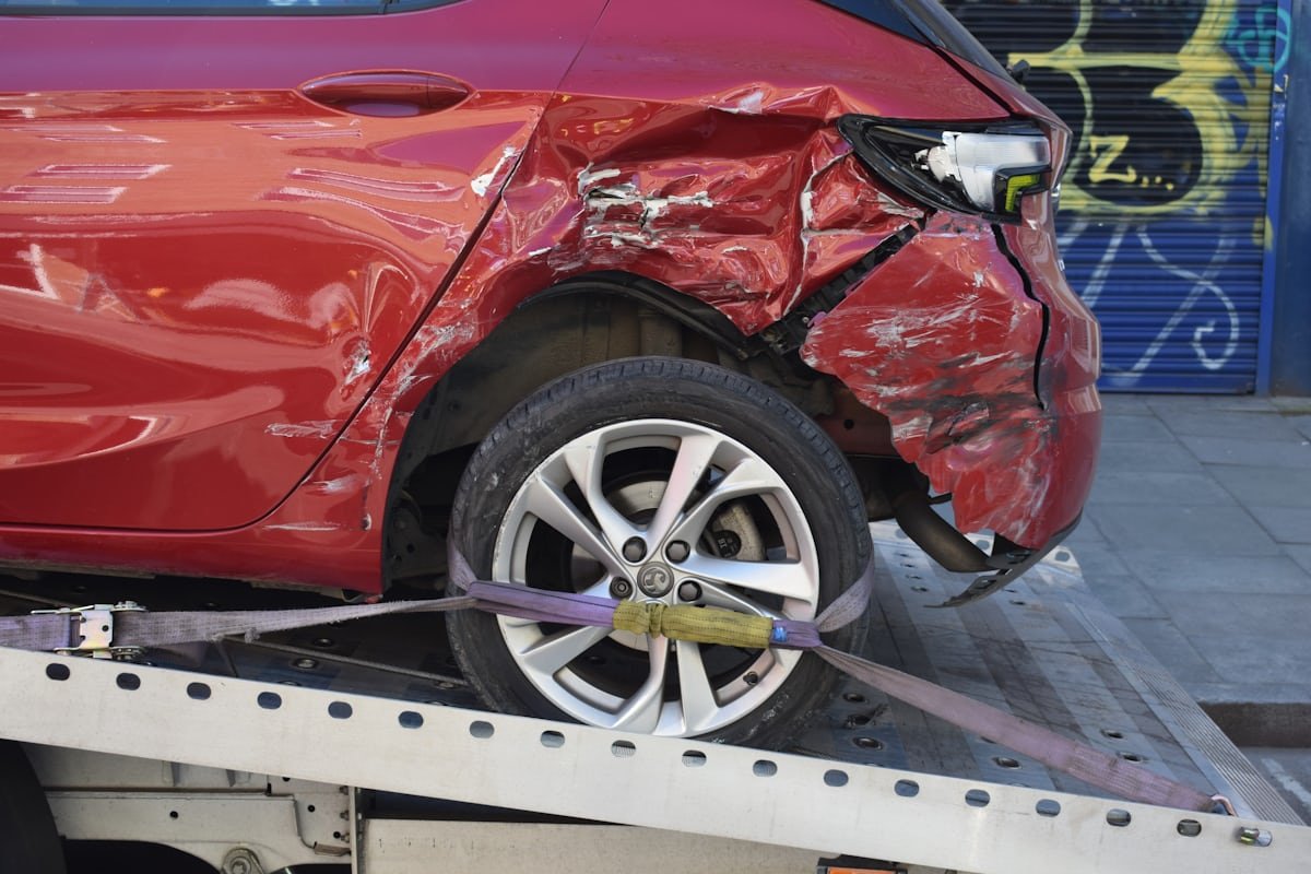 A damaged hatchback with rear-quarter collision damage secured on a flatbed tow truck